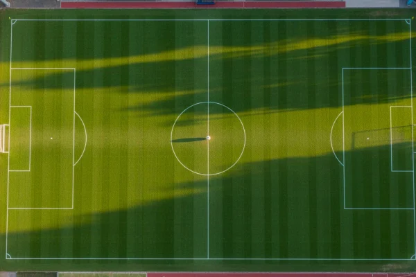 Campo de futebol relvado visto de cima com linhas brancas e bola ao centro